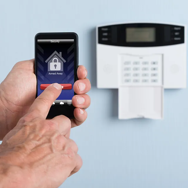 Hånd holder mobiltelefon som styrer et hjemmealarmsystem.